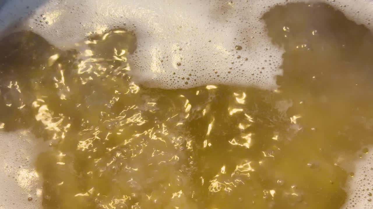 Un primo piano dall'alto mostra della pasta che bolle rapidamente in una pentola con della schiuma bianca