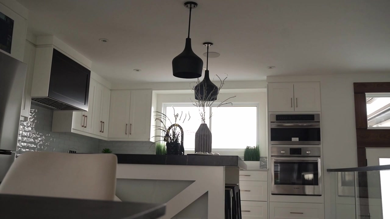 A slow lateral move reveals a still white kitchen with an island, dark countertops and pendant lights. Soft daylight creates a calm setting for kitchen design and real estate content.