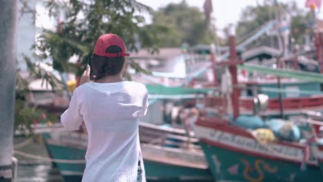 brunette-tourist-takes-photos-of-boats-against-green-trees