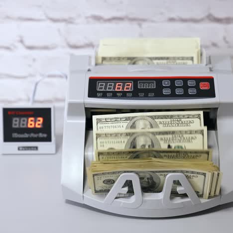 us dollar bills. woman putting money into counting machine at table indoors, close up