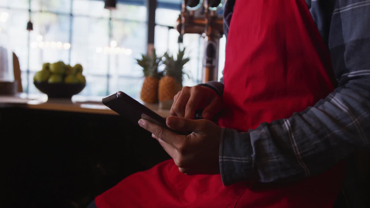 Mixed race male barista wearing an apron using a smartphone