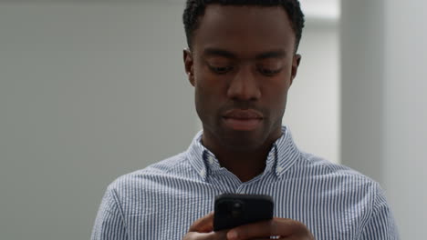 close up of young businessman walking along corridor in office towards camera messaging on mobile phone