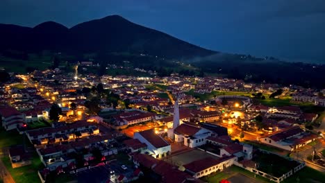 guatavita, colombia at dusk, with warm village lights glowing beneath a looming dark mountain backdrop.