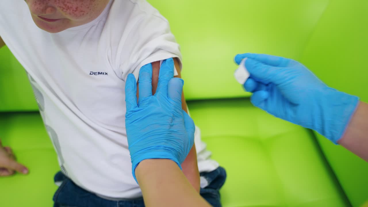 Female doctor doing an injection. Nurse worker in blue sterile gloves pricking needle into boy's arm. Medical procedure of injection. Close-up.