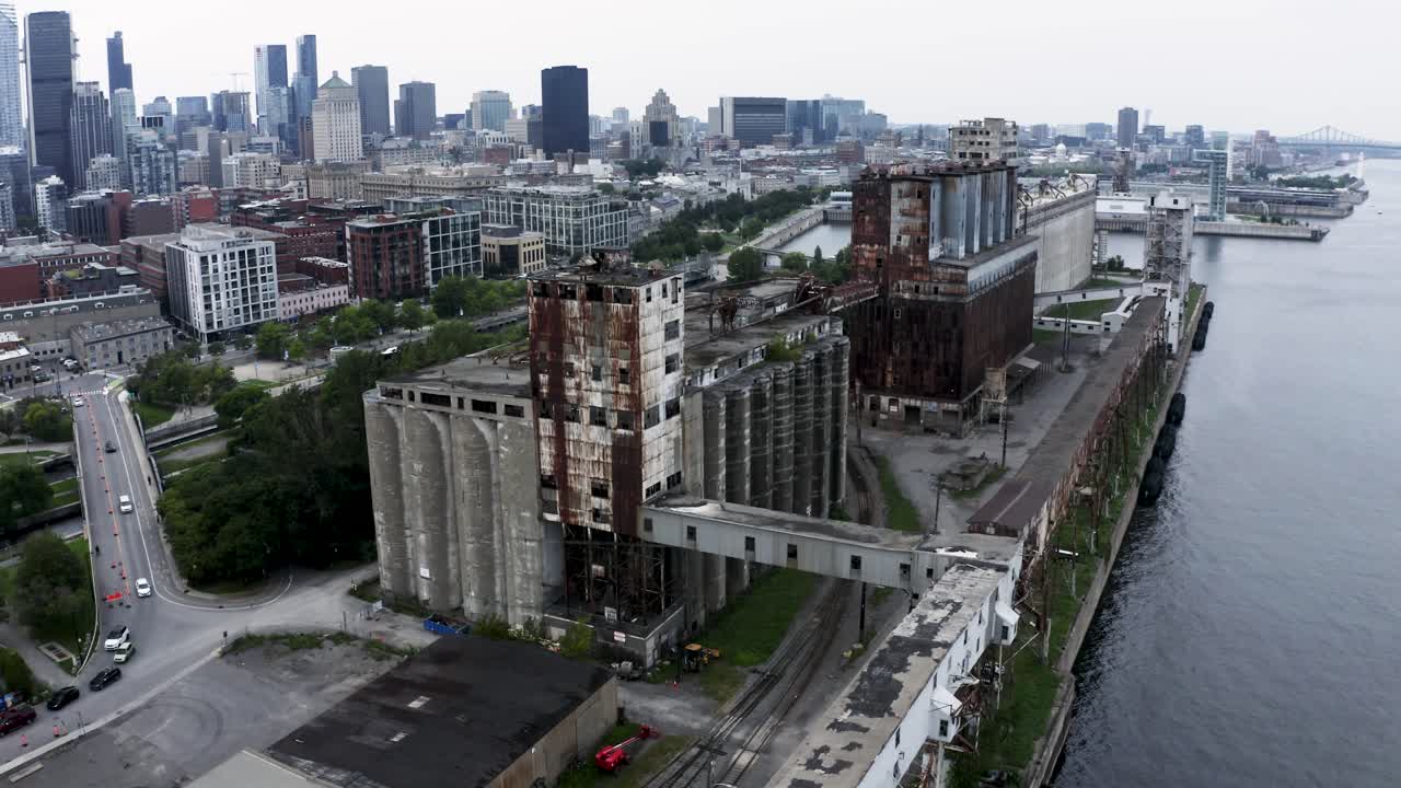 Aerial view of rusted industrial silos with a modern city skyline backdrop. A stunning contrast of urban decay and sleek architecture. Montreal's Old Port docks.