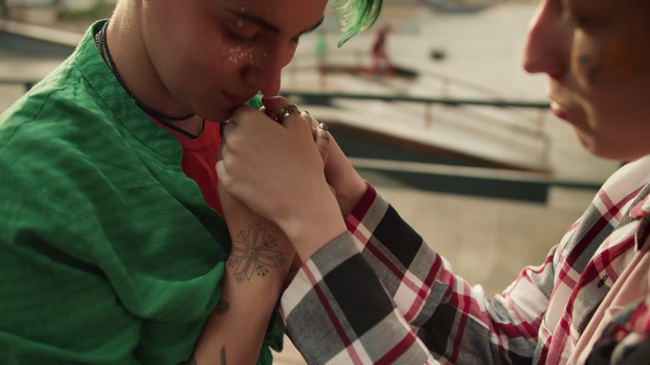 fotografía de cerca de una chica con una camisa verde besando las manos de sus amigas en el parque cerca de la zona de patinaje. pareja de lesbianas en una cita en el parque tomándose de la mano y besándose las manos