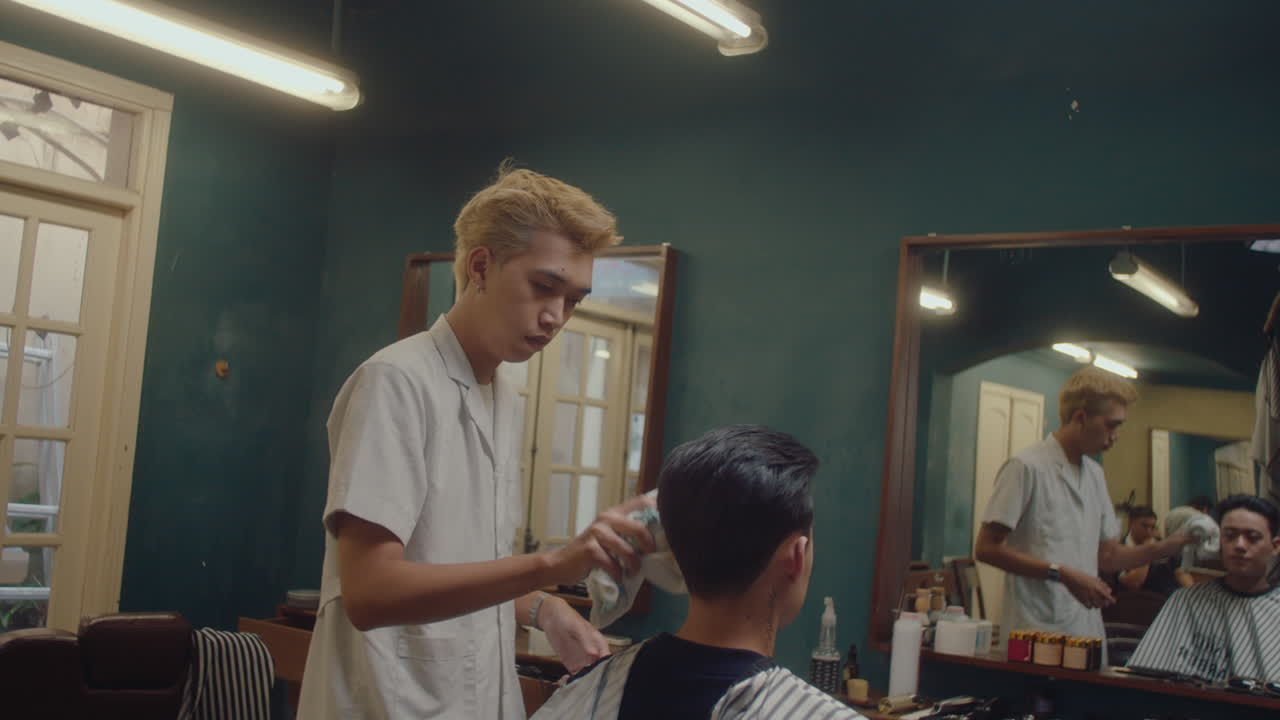 Asiatisk barber afslutter klipningen, bruger håndklæde og tager kappen af