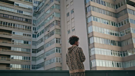 Curly man contemplating city view from building urban expanse. Guy smoking