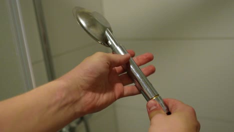 Hands-disconnecting-showerhead-from-its-hose-in-the-bathroom,-static-POV