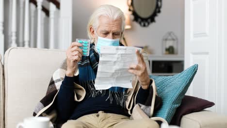 retrato de un anciano con una máscara médica, sentado en casa y leyendo un folleto de información para el paciente mientras sostiene algunas pastillas