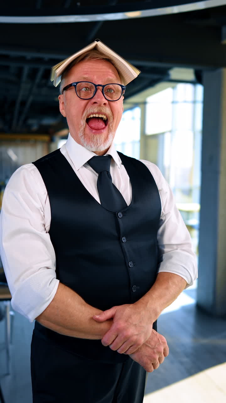 Grey-haired man in official clothes holding a book on his head. Man going crazy from lots of work, making faces in front of camera. Vertical video.