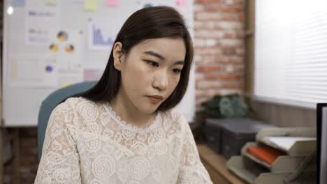 과도하게 일하는 아시아 사업가 여성이 사무실에서 일하는 동안 얼굴에 고통스러운 표정으로 한 어깨 근육을 마사지하고 있습니다.