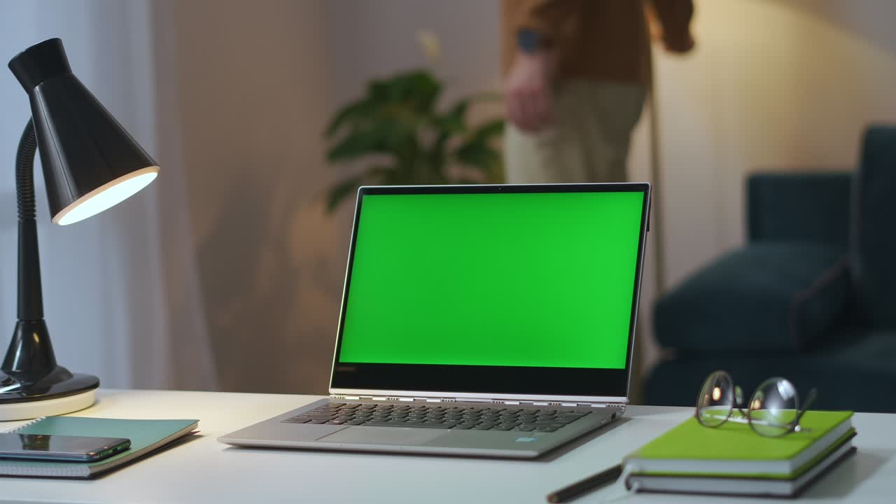 portátil con pantalla verde en la mesa de trabajo en la oficina de casa, el hombre está apagando las lámparas de la mesa y el piso en la sala de estar