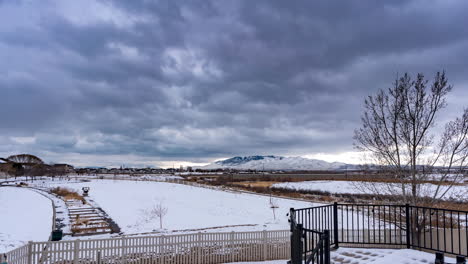 snowy field or park with dark cloudscape above the mountain landscape - time lapse