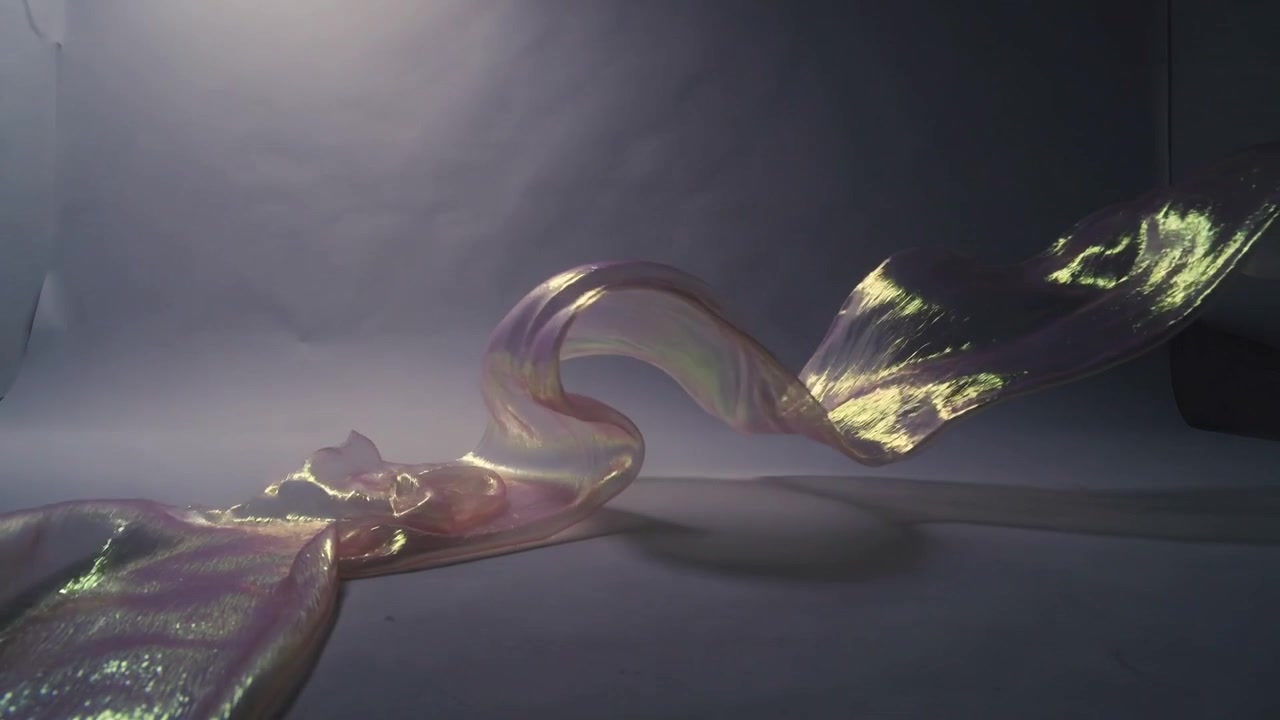 Pulling offframe hand lifting iridescent ribbon across white sweep, forming coils and highlights