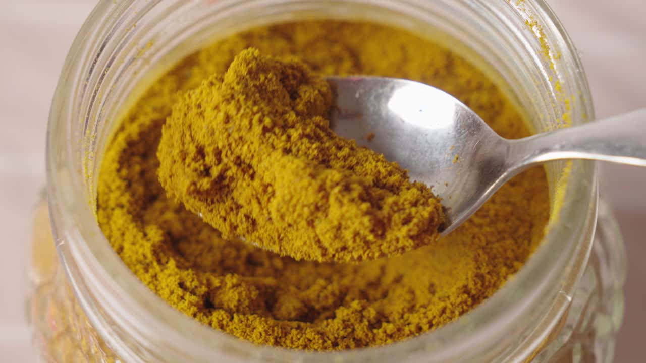 Person picking up a spoonful of dry curcuma from a spice jar