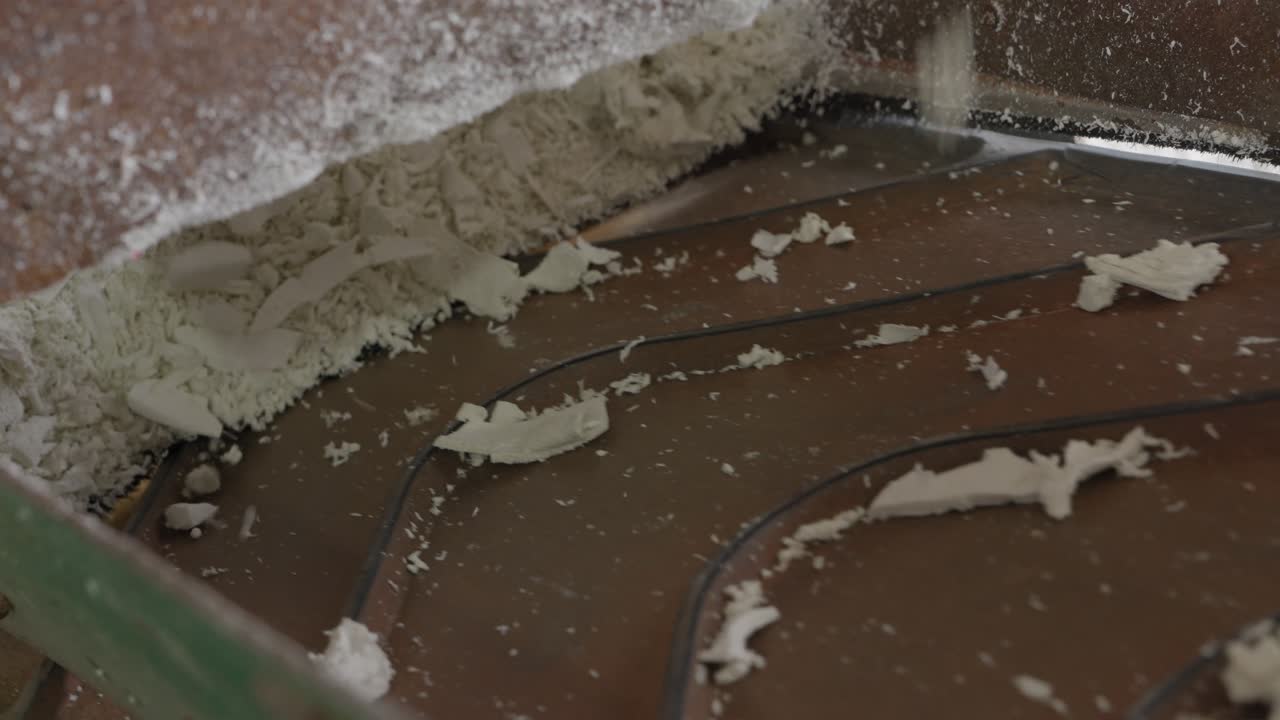 Nærbillede af hvidt plaststøv og flager, der kommer fra en industriel plastkværn.