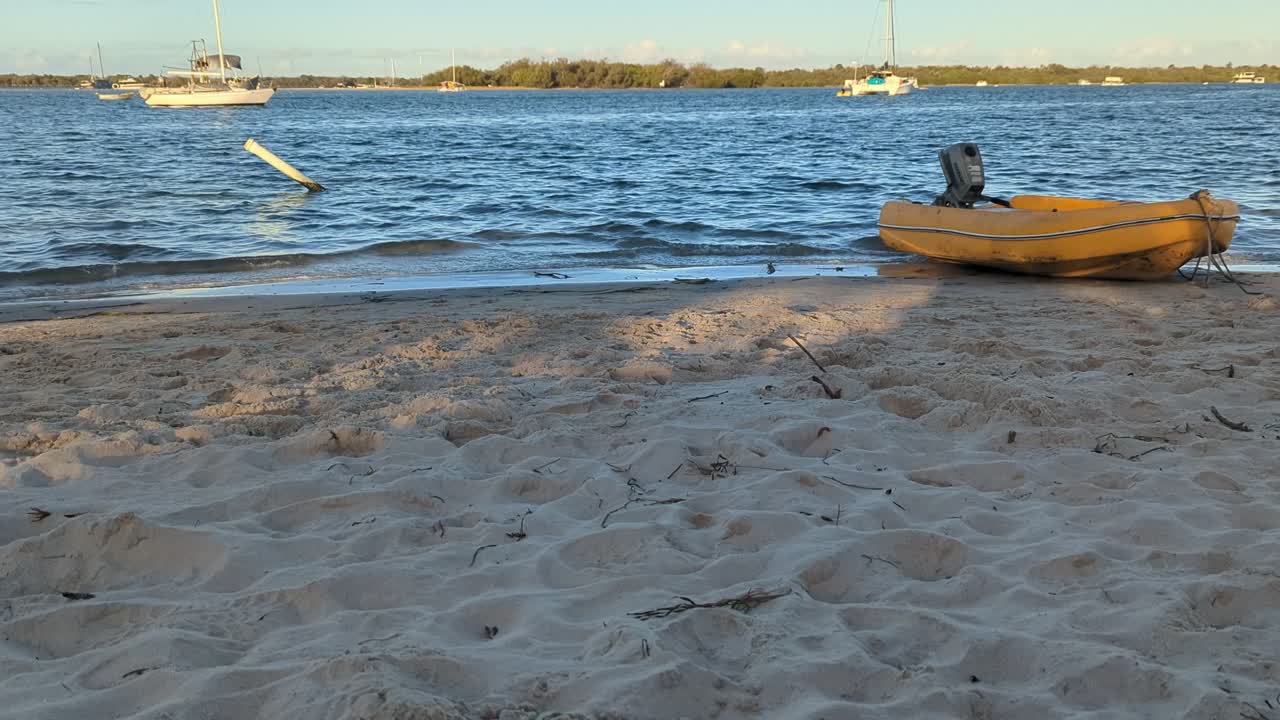 Yellow inflatable boat on the bank of a beach with small waves rolling over the sandy shore.