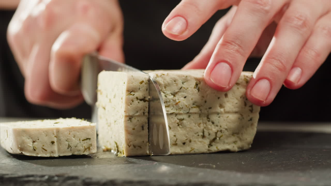 Chef cut cheese for Fried tofu with sesame seeds and spices on cast iron pan, cooking japanese salad. Healthy ingredient for cooking vegan vegetarian diet food. Roasted tofu over black background.