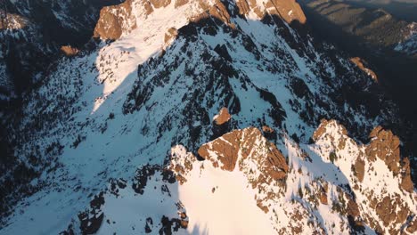 un dron mirando hacia abajo de un pico nevado en las montañas olímpicas tomado desde las afueras del parque nacional al atardecer