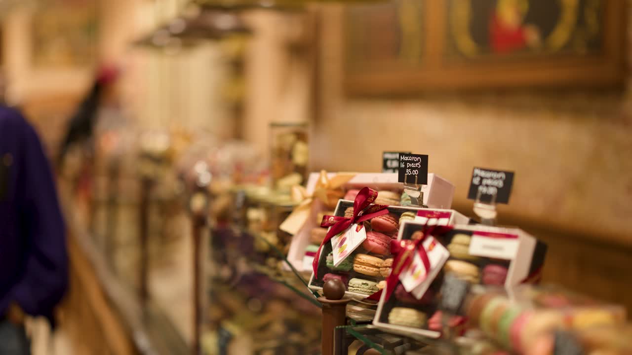Camera slowly pans chocolate shop display window with assorted sweets, pastries, and gift boxes