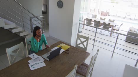 Mujer-Afroamericana-Hablando-Por-Teléfono-Inteligente-Y-Usando-Una-Computadora-Portátil-Mientras-Trabaja-Desde-Casa