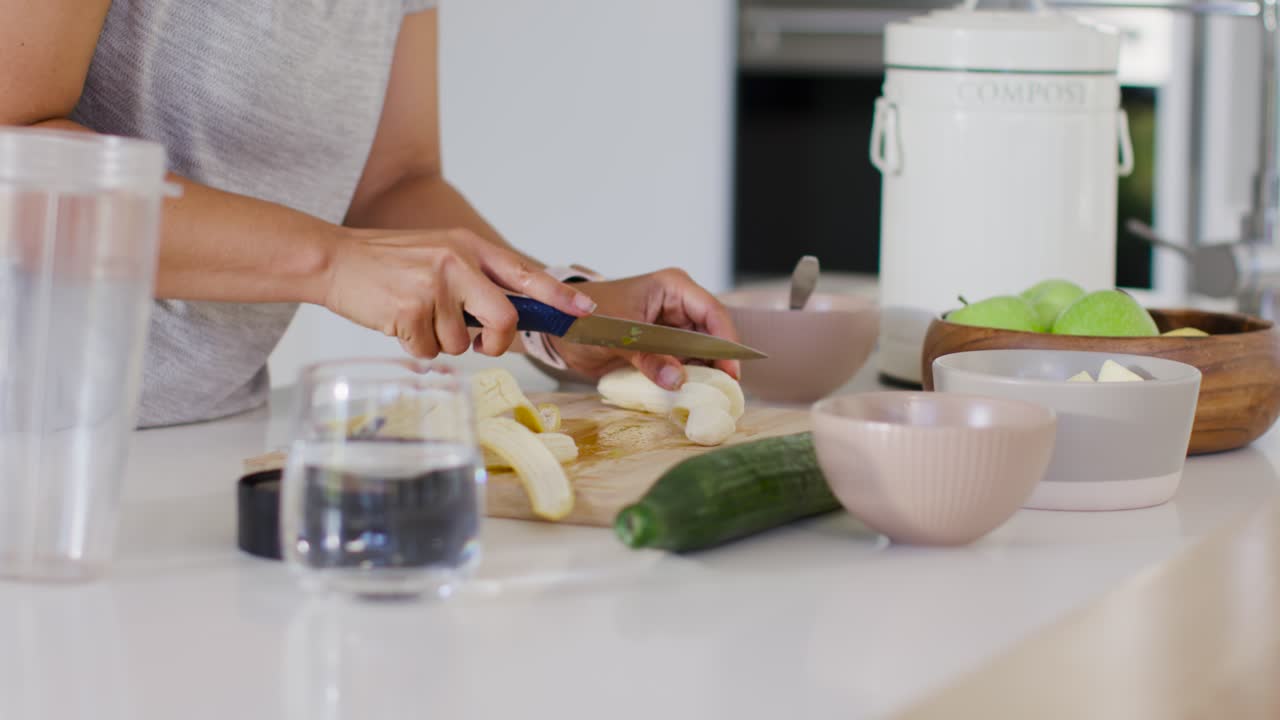 Donna afroamericana che, dopo aver sbucciato una banana, la affetta con un coltello blu su un tagliere, preparando una macedonia.