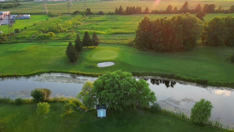 Vista-Aérea-De-Drones-Sobre-El-Campo-De-Golf-Durante-El-Estanque-Al-Atardecer-Y-La-Vegetación-Verde-Fresca