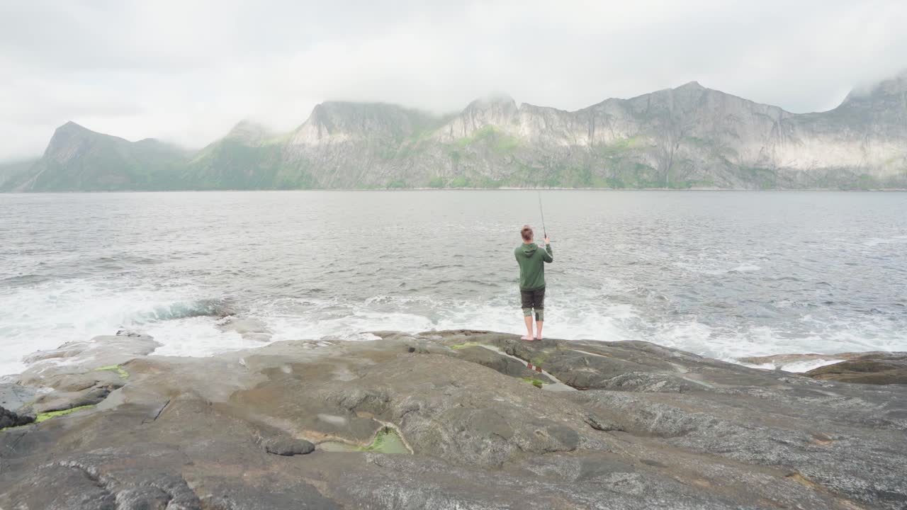 낮에 바다에서 낚시하는 바위 해안의 청년