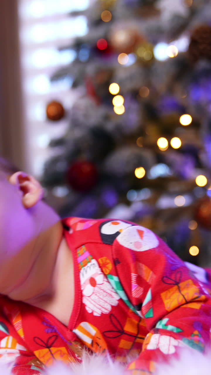 Beautiful child lies near Christmas tree on a plaid. Little infant kid looks up and then falls to his side raising his hands up. Vertical video