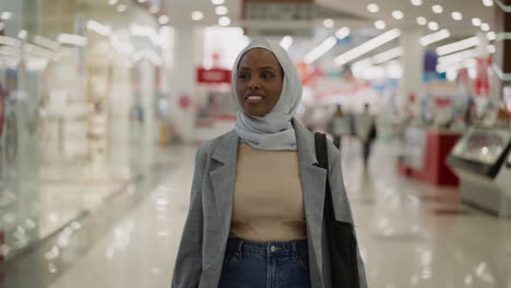 black woman in hijab looks at phone smiles with news in mall