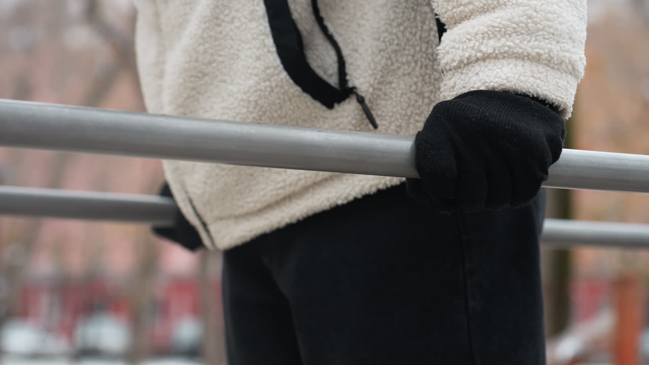 색 겨울 재과 검은 장갑을 입은 개인이 야외에서 푸시업을 수행하는 측면 뷰, 흐릿한 겨울 배경과 추운 날씨에 는 사람들의 불분명한 인물