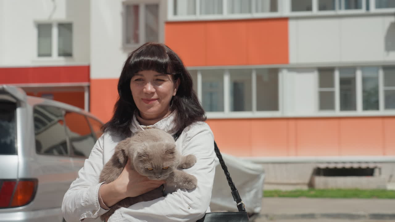 Female Holding Pet Outside Apartment Building, Woman Gently Cradles Cat Beside Parked Vehicle During Morning, Lady Standing Near Vehicle Outside Residence With Feline In Her Arms At Dawn
