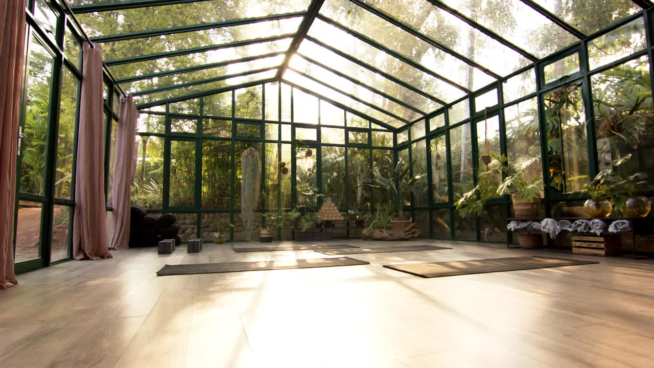 Practicing yoga in glass house with mats, surrounded by lush greenery