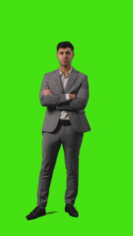 Vertical-Video-Full-Length-Shot-Of-Businessman-Standing-Against-Green-Screen-Folding-Arms-And-Putting-Hands-In-Pockets-Against-Green-Screen