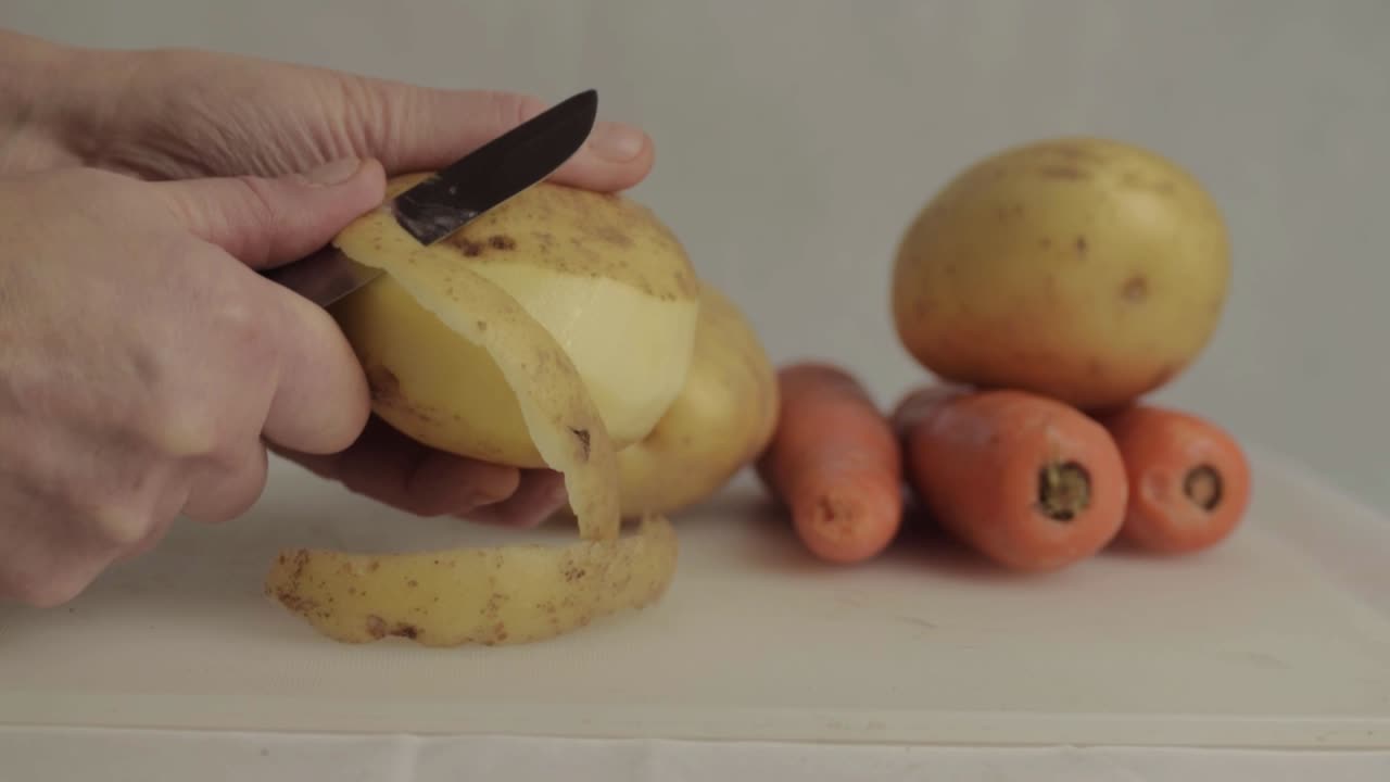 Hands peeling potatoes with carrots in background medium shot