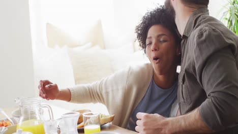 Video-of-happy-diverse-couple-eating-breakfast-and-talking-at-table