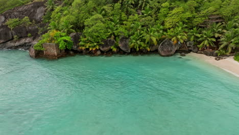 Aerial-view-of-small-exotic-beach-surrounded-by-green-lush-vegetation-in-the-Seychelles