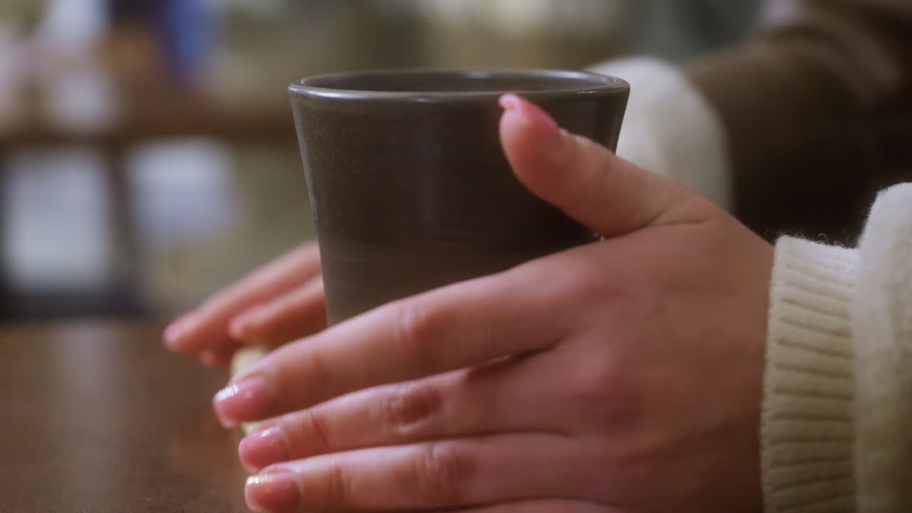 Close-up of hand gently placing cup of coffee on wooden table in cozy cafe, creating calm, inviting atmosphere. Soft light and blurred background enhance relaxed, peaceful vibe of setting