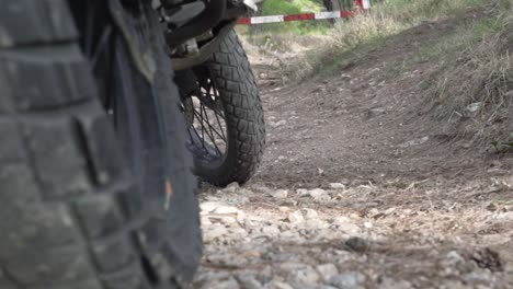 close up on motorcycle wheels, static on soil ground, pull focus from wheels to road barrier in the background 120fps