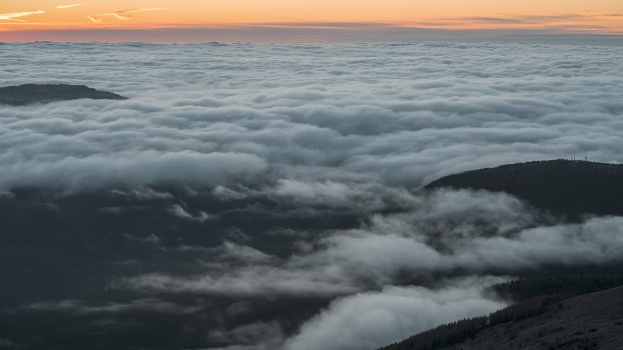 por encima de las nubes al amanecer con tonos cálidos del cielo y silueta de la montaña, time-lapse