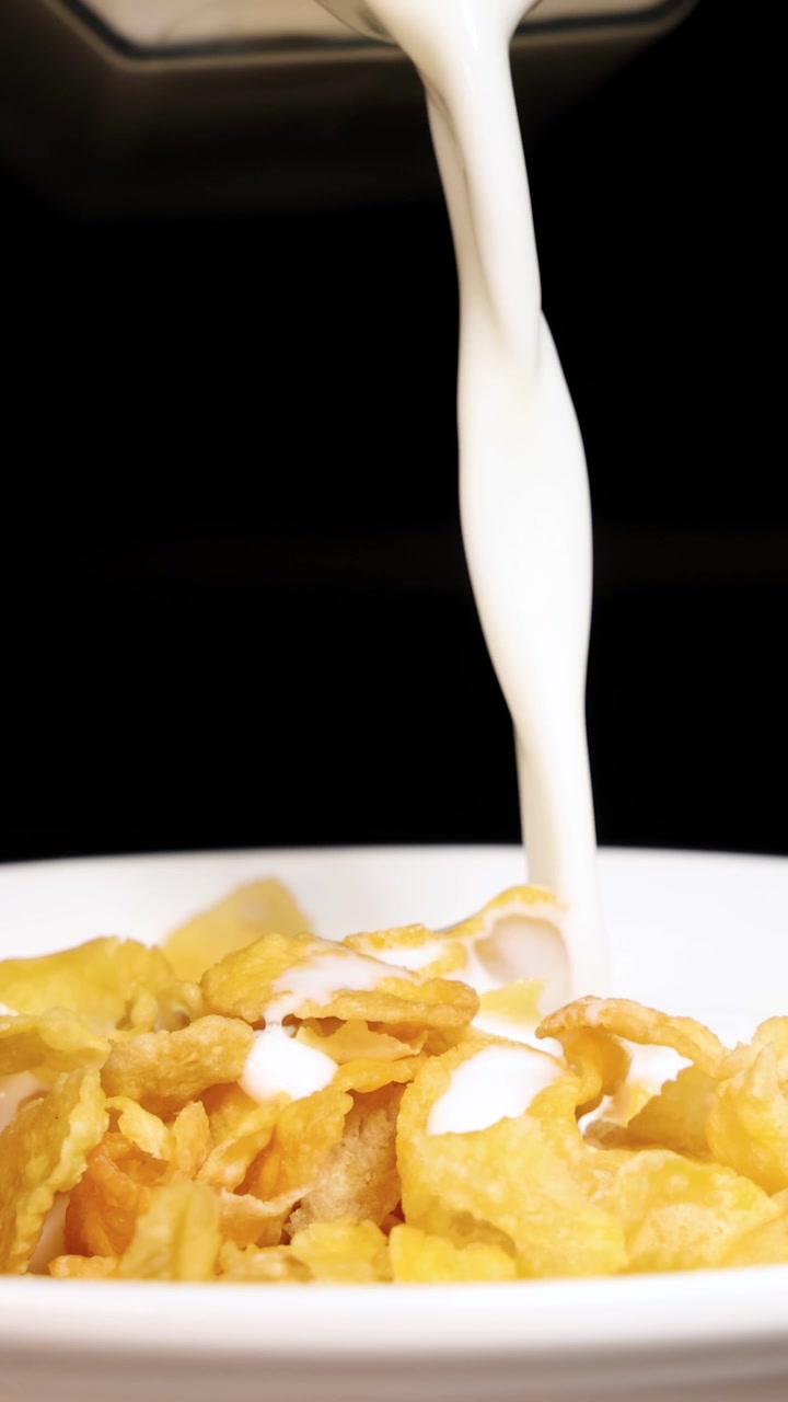 Il latte viene versato su cereali di mais croccanti in una ciotola su uno sfondo nero, creando una dinamica scena per la colazione.