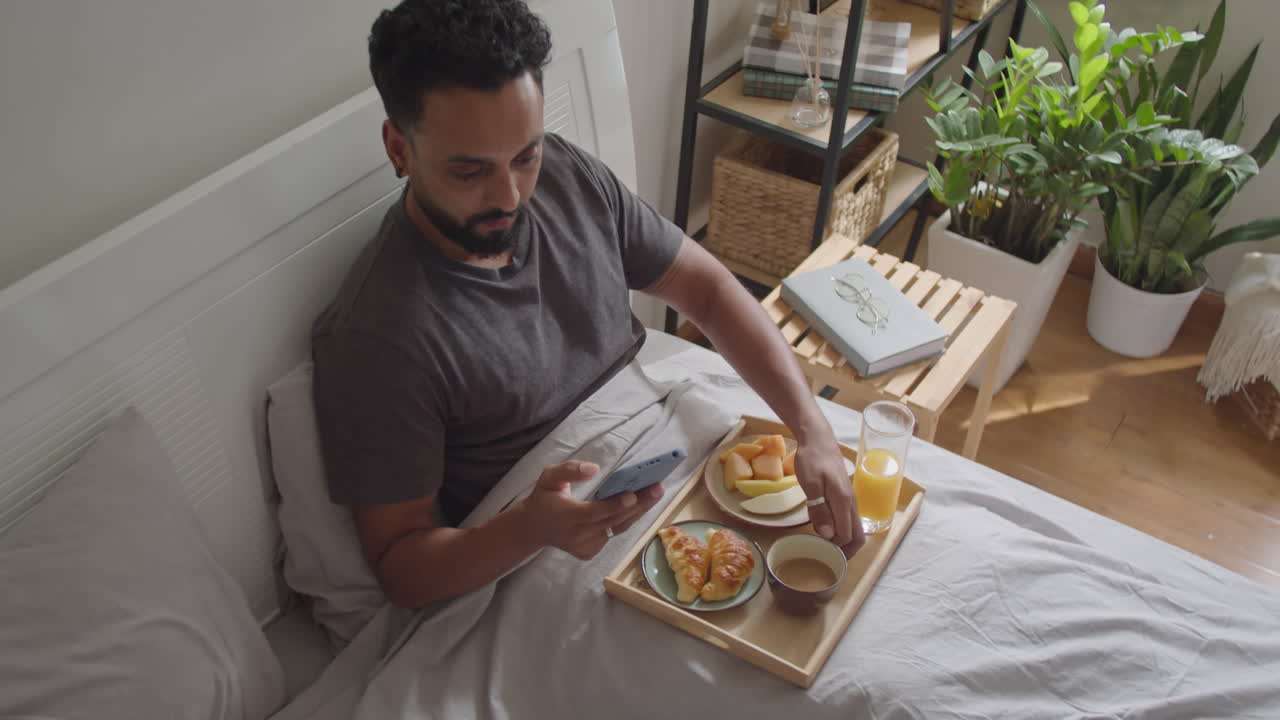 Man Using Mobile Phone and Having Breakfast in Bed