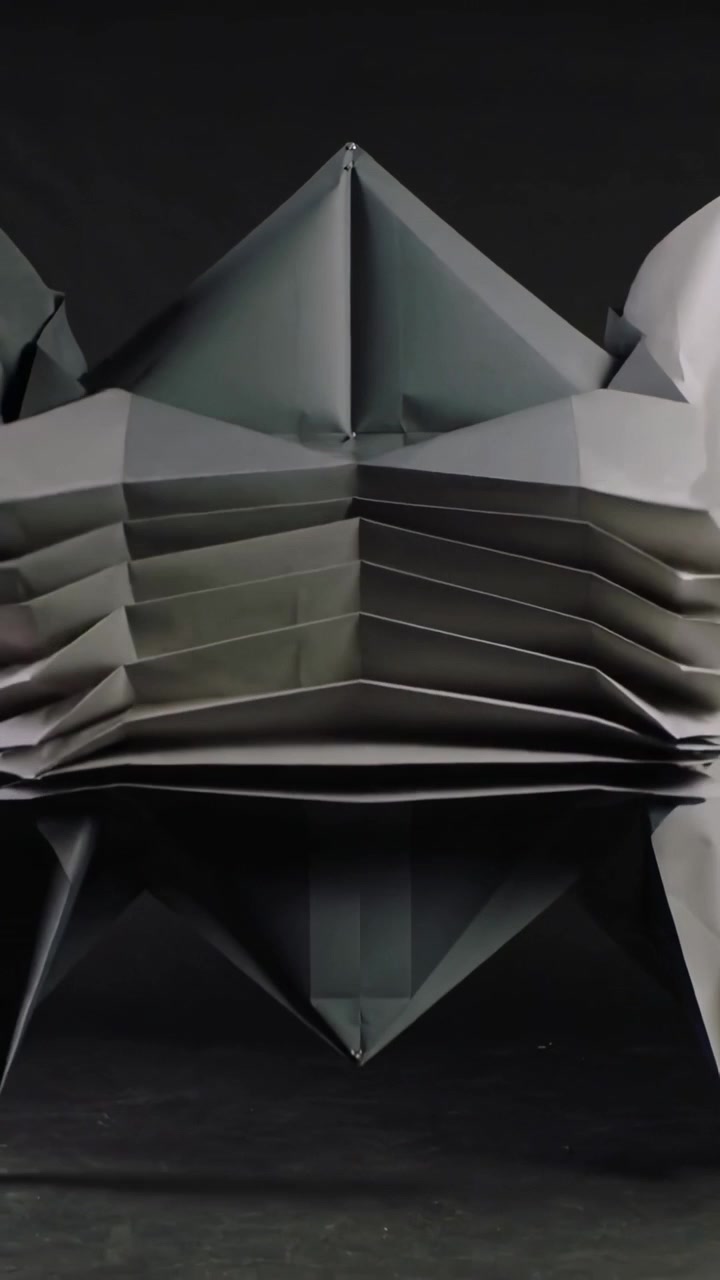 Vertical video: Folding dark sheet by center pinch, forming fan pleats into art on table with pin
