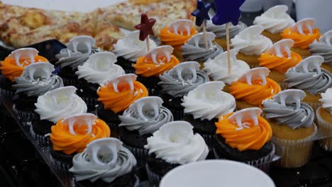 generic boxed cupcakes for kids birthday party event on shaking table with cheese pizza and white single use styrofoam cups in background as a fly flies by - in cinema 4k (30fps slowed from 60fps).
