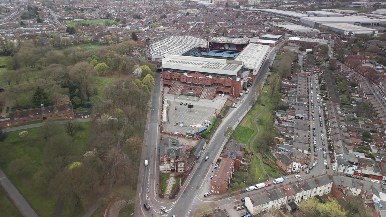 Aston Villa F.C. stadium rises above Birmingham streets, homes and parkland in an aerial city view.