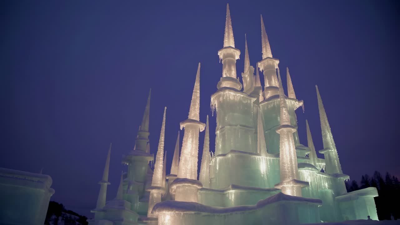 A low-angle video shot of a majestic ice castle, illuminated against a twilight sky
