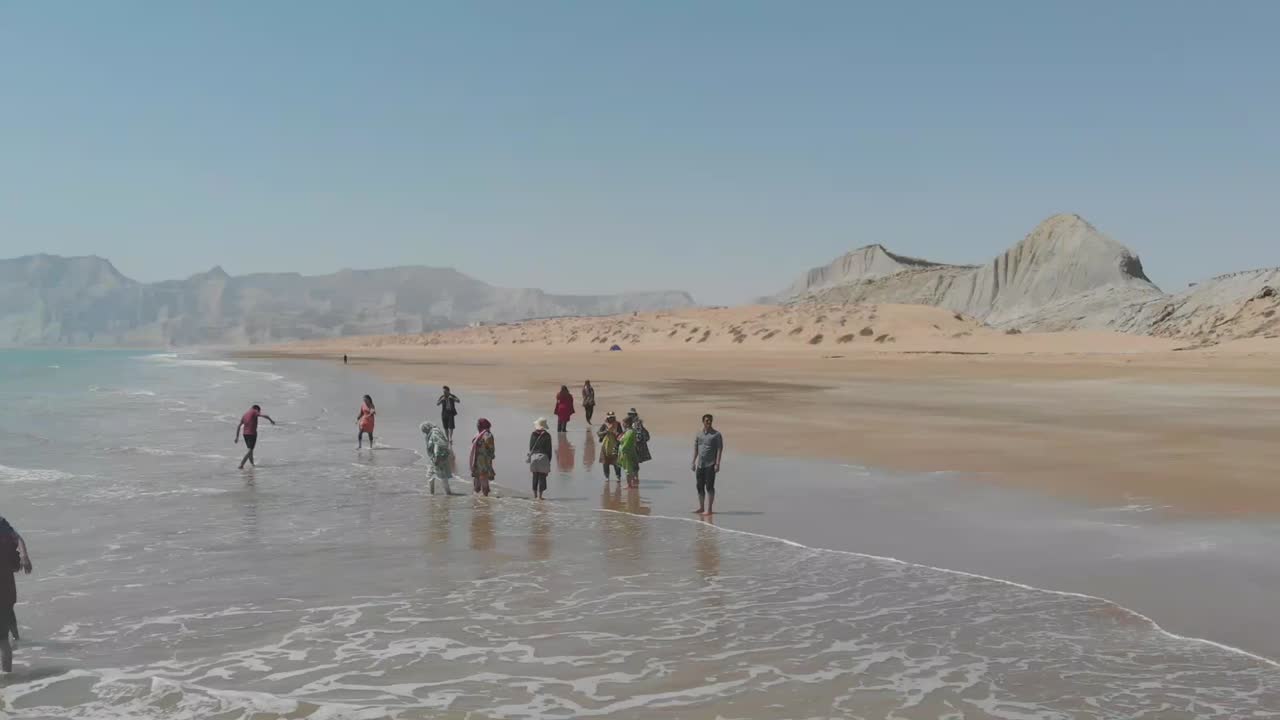Family Enjoying Wading In Water On Golden Beach In Balochistan. Aerial Follow Shot