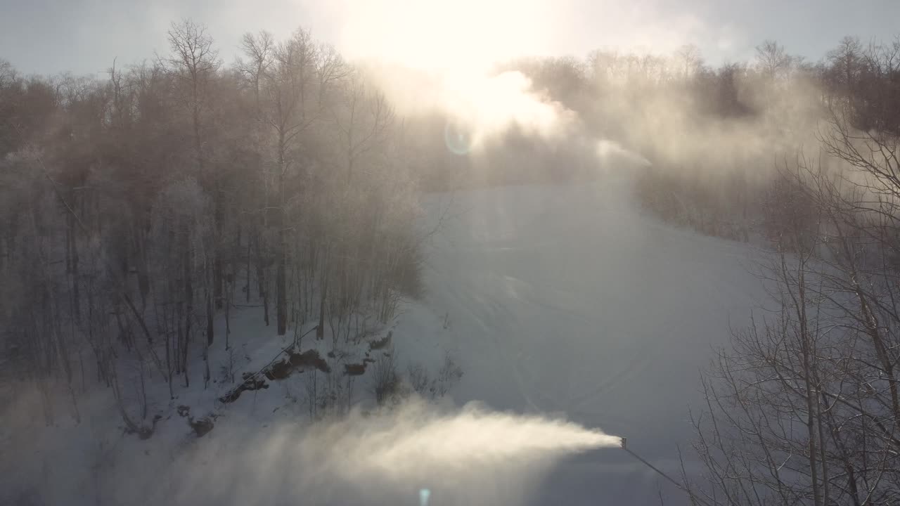 Machines producing snow on ski track on sunny day, aerial view