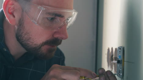 el constructor con gafas de protección instala el enchufe en la pared de la habitación vista de cerca